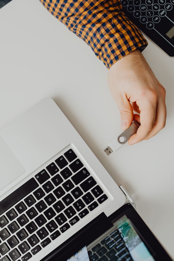 Hand inserting USB flash drive into a laptop, view from above.