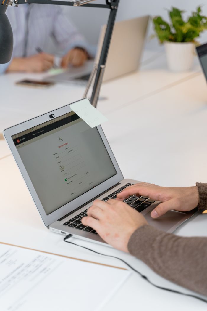 Close-up of hands typing on a laptop in a modern office with coworkers in the background.