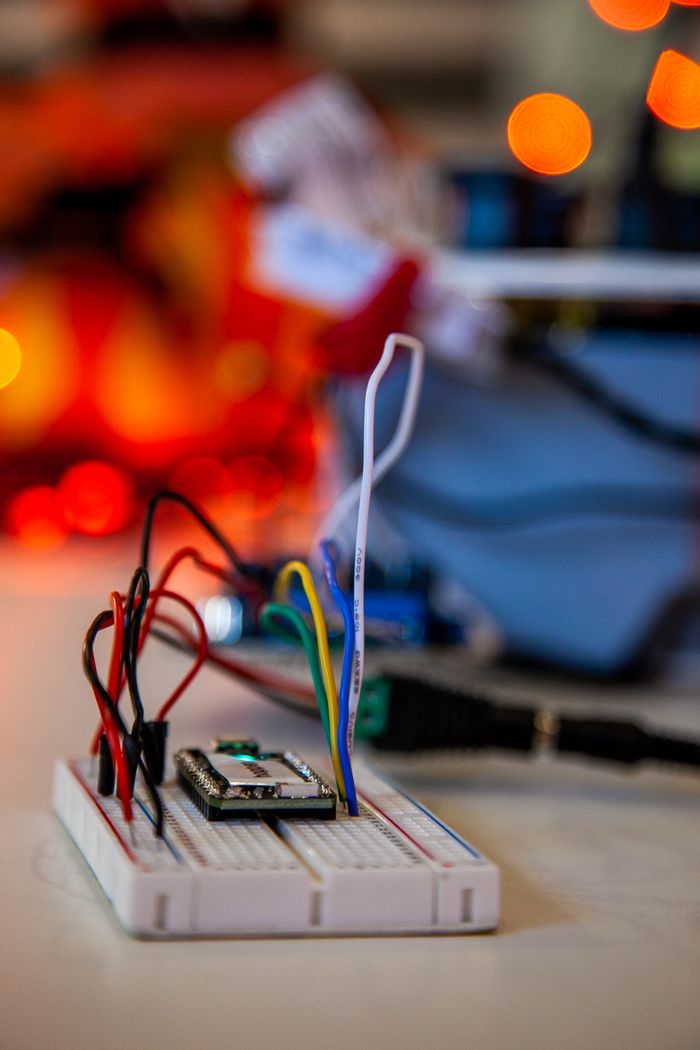 Detailed close-up of electronics breadboard with colorful wires and blurred lights in the background.